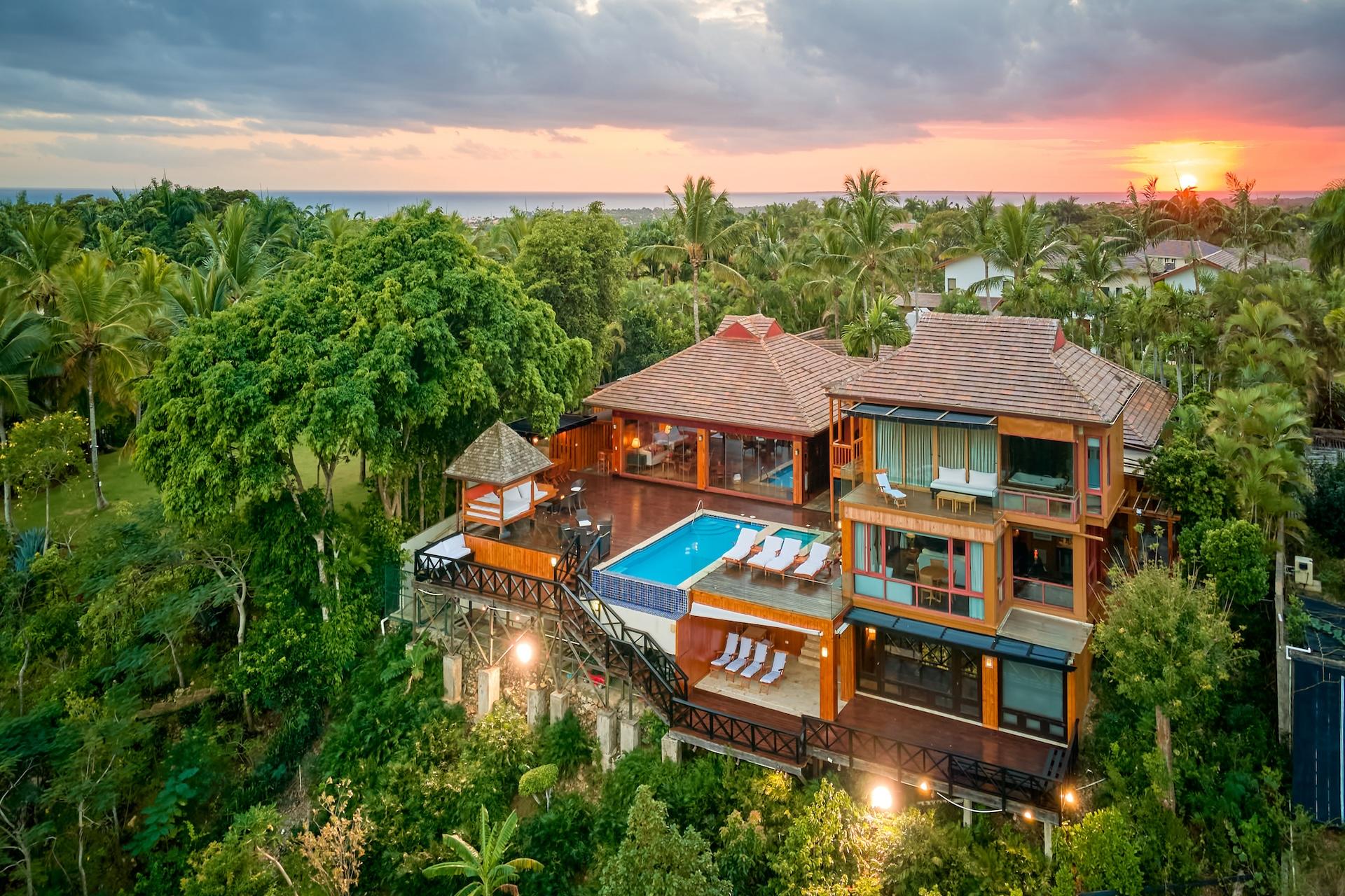 Aerial sunset view of the multi-level wooden villa with pool and tropical gardens above the Chavón River