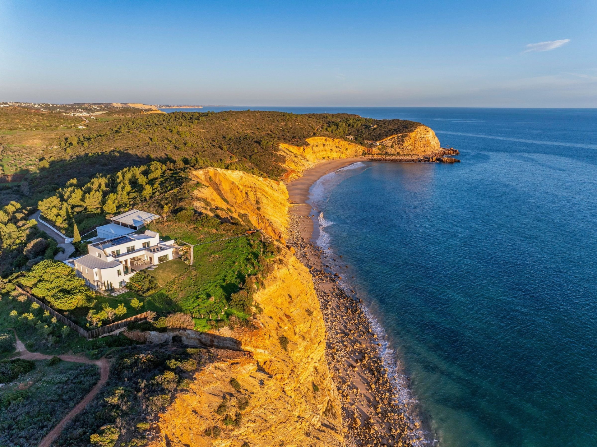Aerial View of the White Villa perched above Golden Cliffs and a Sandy Cove