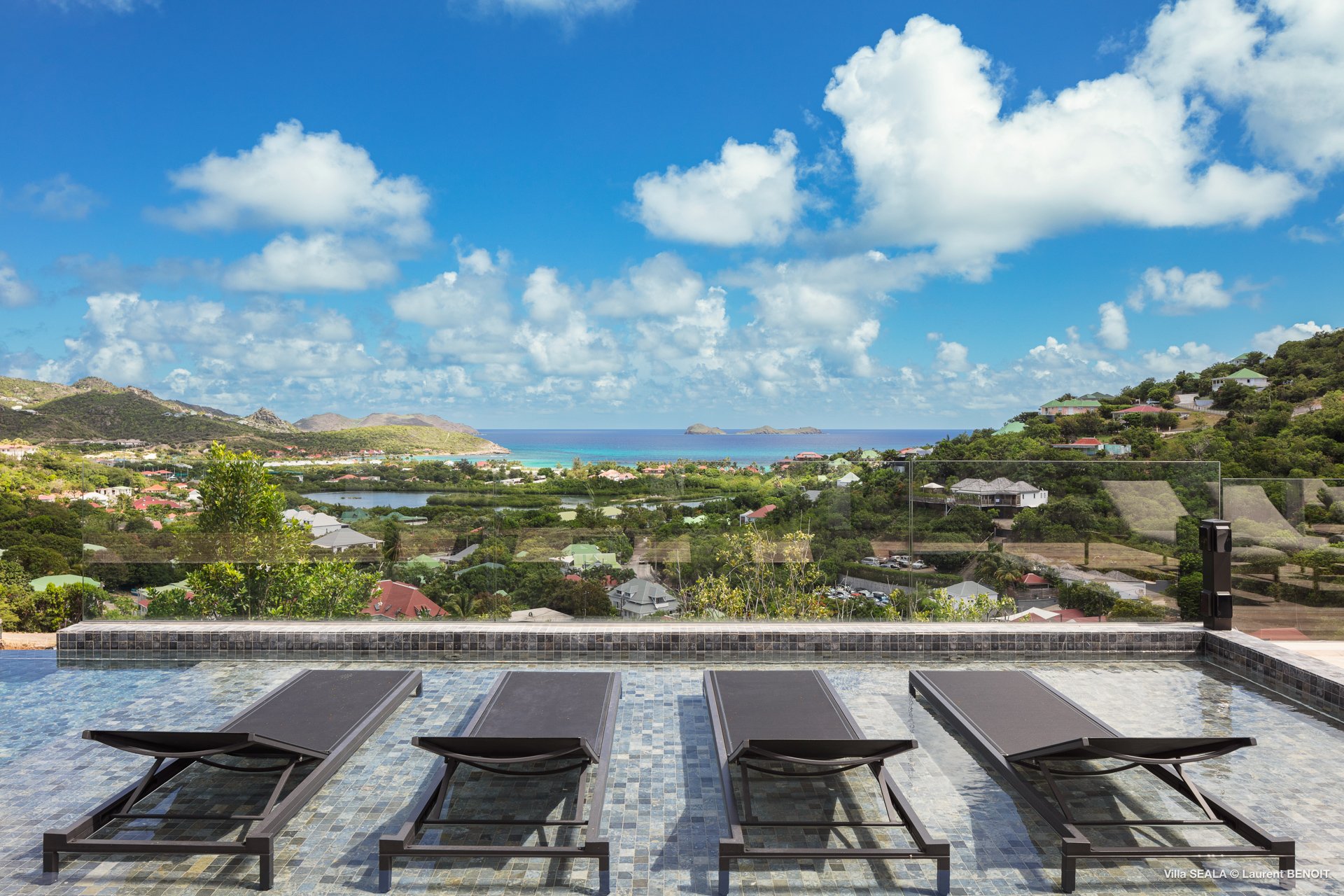 Infinity pool terrace with four loungers overlooking Saint Jean Bay and green hills